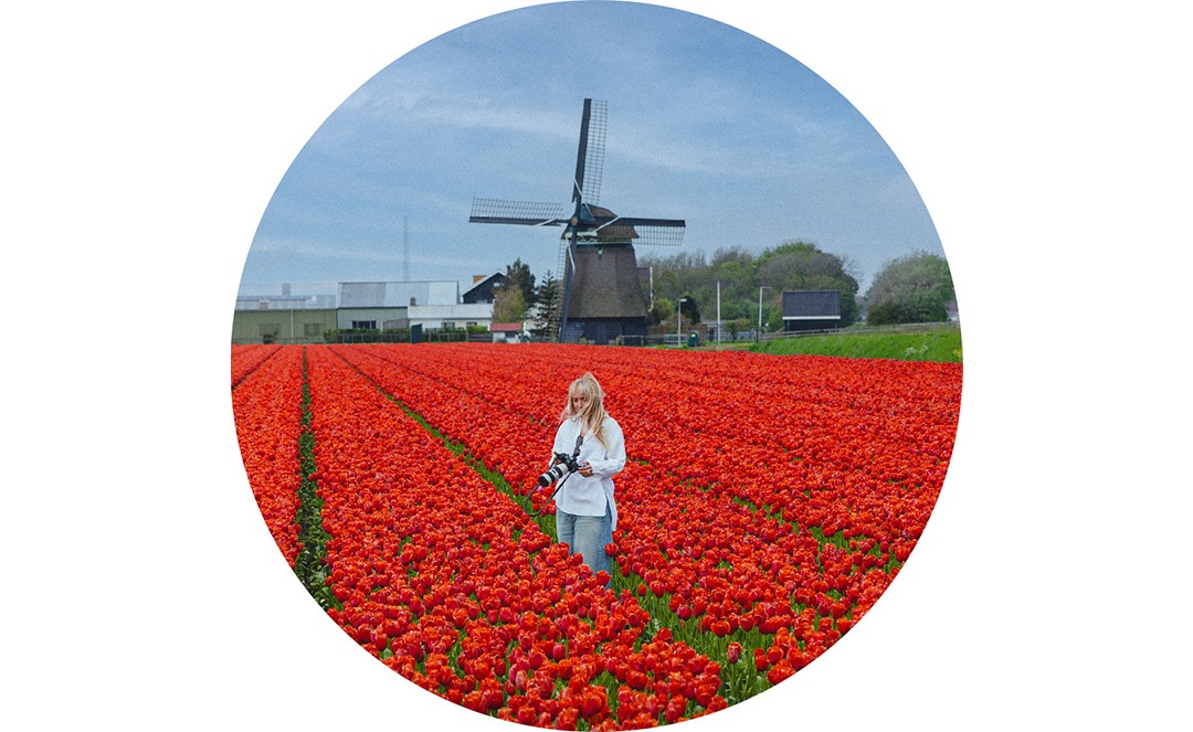 Holding a professional camera, Katarina Višekruna stands in a field of red-orange tulips.